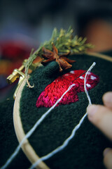 Woman hands doing stitch. Process of embroidery of mushroom hat in wooden hoop on green material. Concept of needlework diy, hobby, leisure.