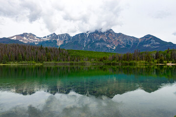 Patricia Lake in Jasper Alberta, clear water with reflection of Pyramid Mountain. White partially cloudy sky