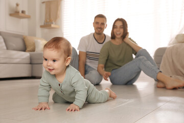Happy parents watching their cute baby crawl on floor at home