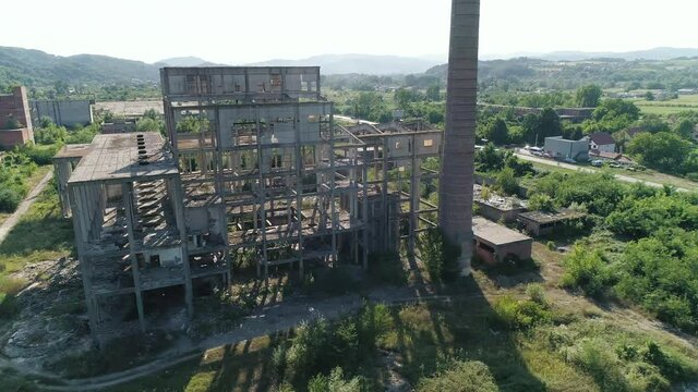Exterior abandoned factory complex in Loznica Serbia Chimneys aerial drone shot. Flight orbit around skeleton of ex factory hall. Urban exploration of abandoned place chemical plant. Nature takes over