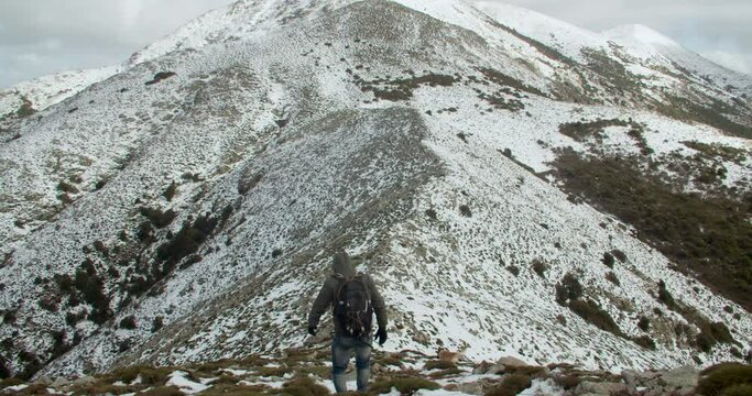 Rear view of mountain climber on top of snowy white Monte Linas peak in Sardinia followed by german Sheperd dog, Italy, wide shot, zoom in
