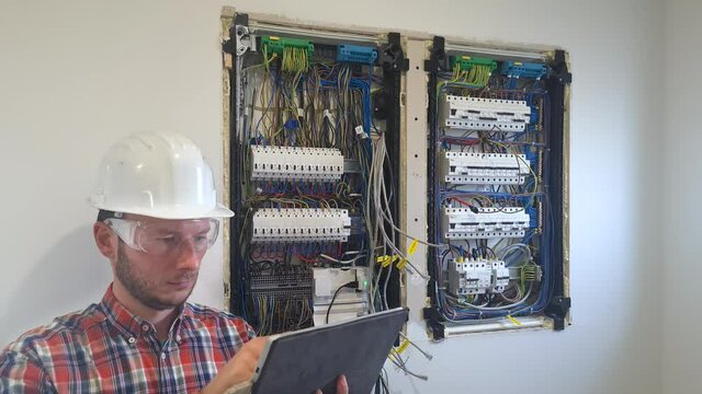 Professional technician repair and maintenance switchboard in electrical cabinet and controlling the process with external iPad tablet device