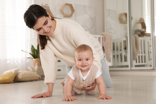 Happy young mother helping her cute baby to crawl on floor at home