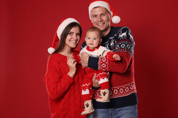 Happy couple with cute baby in Christmas outfits and Santa hats on red background