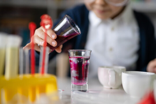 Close up on hand of One small caucasian boy scientist five years old sitting at the table playing with chemistry equipment toy preforming experiment learning and education concept front view