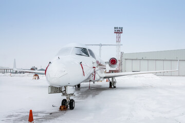 White luxury corporate business jet near the airplane hangar in cold winter weather