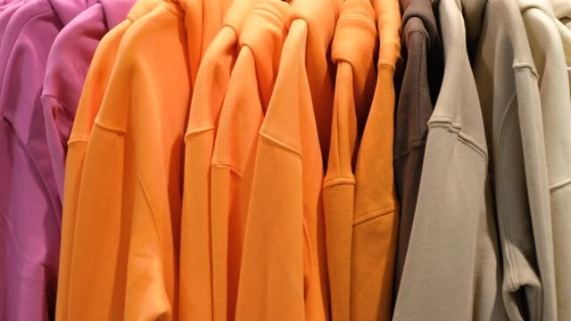 Bright hoodies of different colors rotate on a hanger in a store, close up.