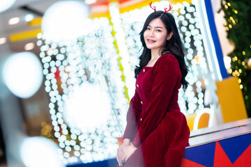 Portrait beautiful young asian woman red dress costume and Christmas greeting picture parcel decoration on Christmas tree light circular bokeh background Decoration During Christmas and New Year.
