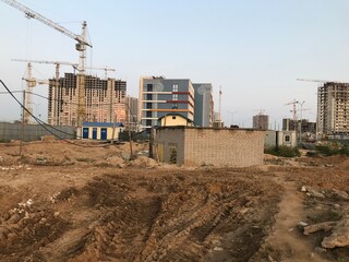 dirt at a construction site. sand furrows, tracks from heavy vehicles. there are houses nearby, a booth with transformers. construction landscape