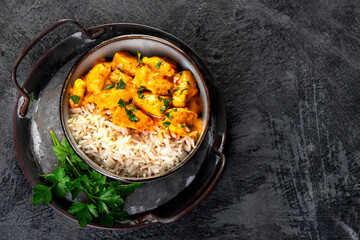 Indian butter chicken curry with basmati rice on dark background.
