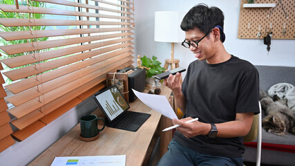 Smiling asian man working with financial documents and talking on mobile phone.