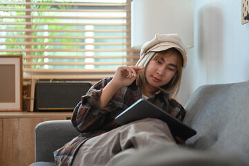 Obraz premium Young asian woman sitting on comfortable couch and using digital tablet.