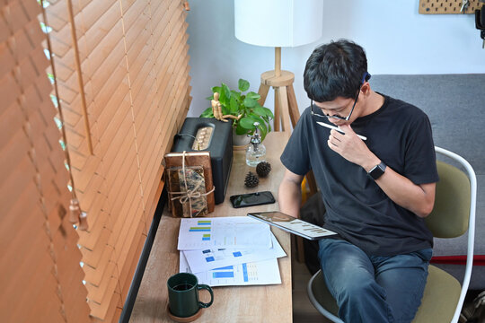 Thoughtful asian man analyzing financial data on digital tablet at home.