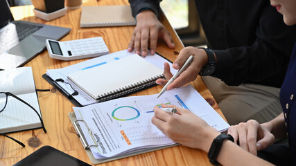 Cropped shot two business people analyzing financial graphs and statistics documents together.