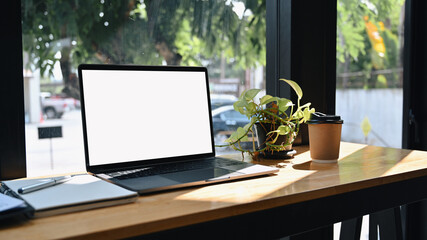 Computer laptop with white screen, notebook and houseplant on wooden table.