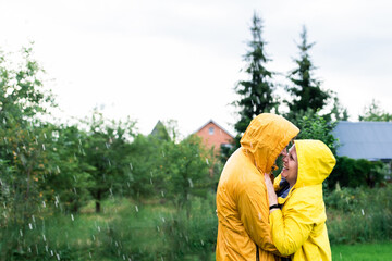 A married couple in yellow raincoats in the rain in their backyard. Front view.