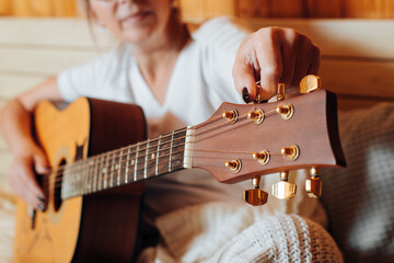 Close-up of woman musician playing an acoustic guitar, tuning musical instrument using peg on...