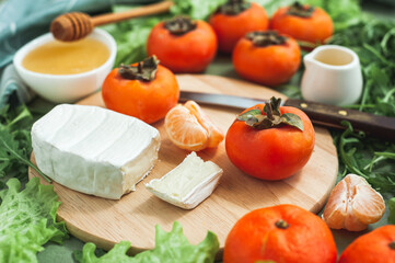 Ingredients and the process of making a vitamin winter salad with persimmons, tangerines and cheese. Selective focus. Dietary nutrition