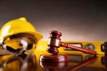 Labour law and builiding law concept.  Gavel and yellow crash helmet on the shining lawyer desk.