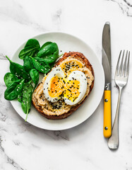 Whole grain grilled bread hummus, boiled egg, sesame sandwich and fresh spinach on a light background, top view