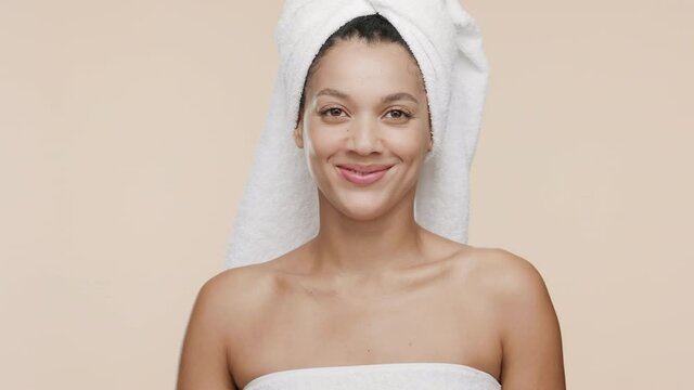 Funny young slim cute African American woman with a towel on her head and bare shoulders throws away orange woman razor smiling wide for the camera on beige background | Unwanted hair removal concept