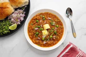 Indian Mumbai Street style Pav Bhaji, garnished with peas, raw onions, coriander, and Butter. Spicy thick curry made of out mixed vegetables served with pav over white background with copy space.