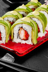 Closeup of uramaki rolls with shrimp, tobiko, avocado and mayonnaise on red plate