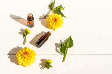 Two glass dropper bottles for medical and cosmetic use and yellow dachlia flowers on a white wooden background. aromatherapy, spa.