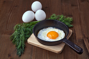 A fried chicken egg in a small frying pan with a stand, a bunch of dill