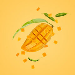Ripe mango fruit sliced with cube and green leaves floating on yellow background.
