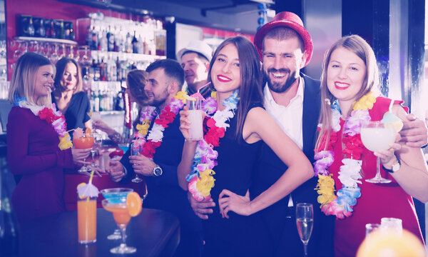 Young man and two women with cocktails having fun on Hawaiian party at nightclub