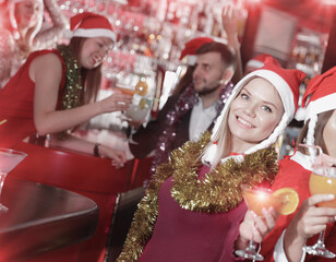 Happy girl in spangle and Santa hat toasting drinks on new year eve party in bar