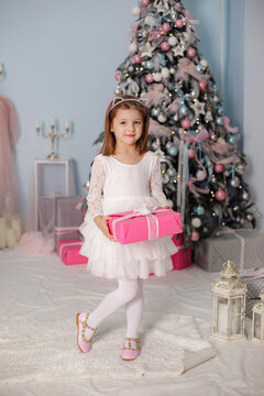 Smiling child girl under Christmas tree with decorations in room.