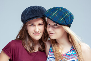 Youth Lifestyle. Two Serious Caucasian Girlfriends Posing Together While Wearing Caps Over White Background.