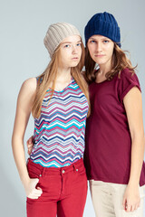 Two Caucasian Girlfriends Posing Together While Wearing Caps And Posing Embraced Over White Background.