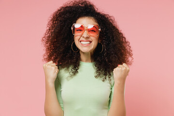 Jubilant excited young curly latin woman 20s years old wears mint t-shirt sunglasses do winner...