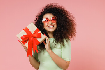 Happy young curly latin woman 20s wears mint t-shirt sunglasses hold shake red present box with...