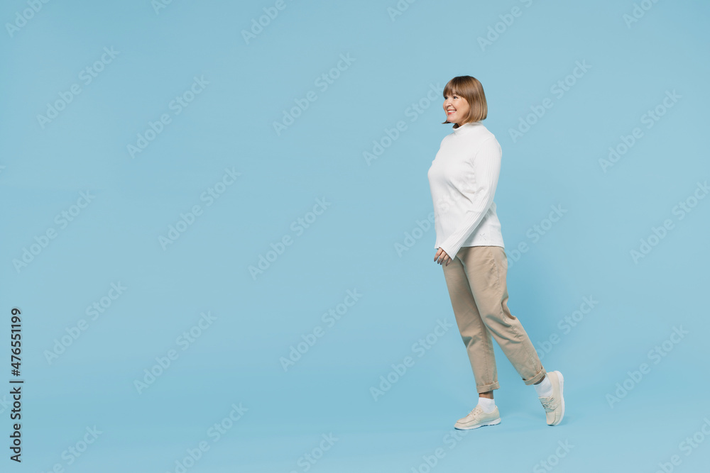 Wall mural full body side view elderly smiling cheerful fun caucasian woman 50s wear white knitted sweater walk