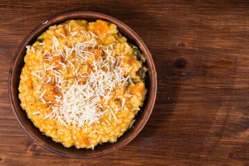 Serving of pumpkin risotto in a plate sprinkled with grated parmesan cheese, top view, copy space
