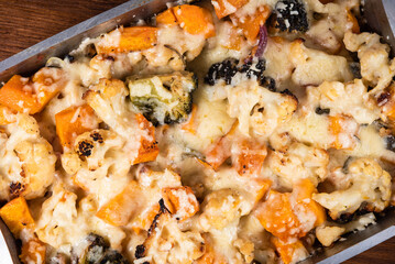 Baked vegetables with cheese in a metal baking sheet - cauliflower, broccoli, pumpkin with onions, top view, close-up
