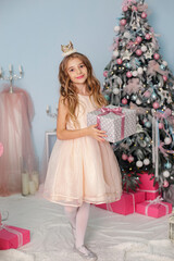 Smiling child girl under Christmas tree with decorations in room.