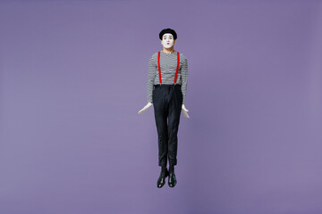 Full size body length charismatic loony young mime man with white face mask wears striped shirt beret jump look camera stand straight isolated on plain pastel light violet background studio portrait.