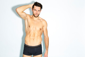 Fototapeta premium Caucasian Handsome Brunet Man in Black Underware In Good Phyisycal Fit While Posing in Underware While Touching Hair Against White