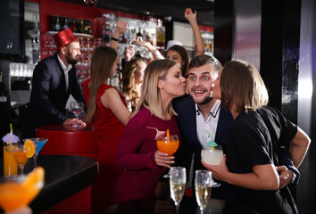 Guy getting friendly kiss on cheeks by attractive girls on cocktail party in bar - obrazy, fototapety, plakaty