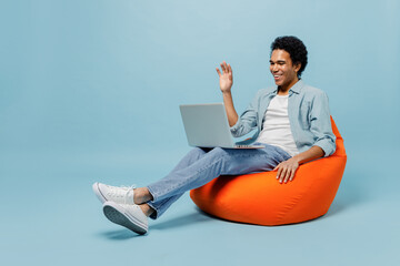 Full size young black curly man 20s wears white shirt sit in bag chair get video call using laptop...