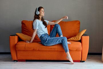 cheerful woman sitting on the couch at home listening to music on headphones unaltered