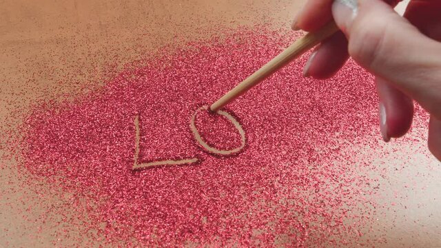 Woman Hand Writes Love . A woman hand writes love on bright red sand.