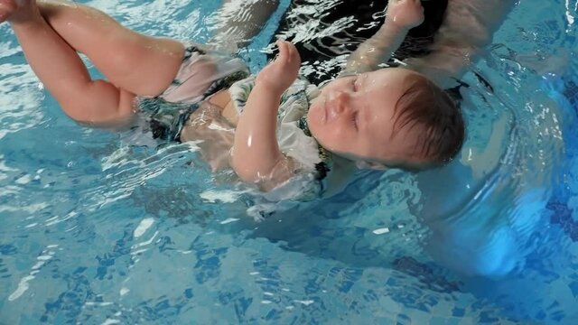 A little one-year-old girl with her mother in a black swimsuit in the pool, a swimming lesson for children. A woman conducts a workout in the pool with a newborn baby.