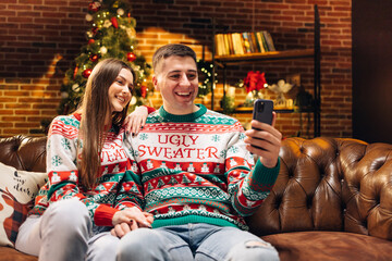 Attractive Man and Woman Talking by Video Call Sending Positive Emotions Looking at Camera. Happy Couple Sitting at Home while Recording Christmas Greetings. Happy New Year. Merry Christmas.