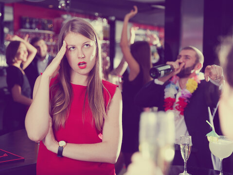 Offended young woman on background with drunk man on party at nightclub.